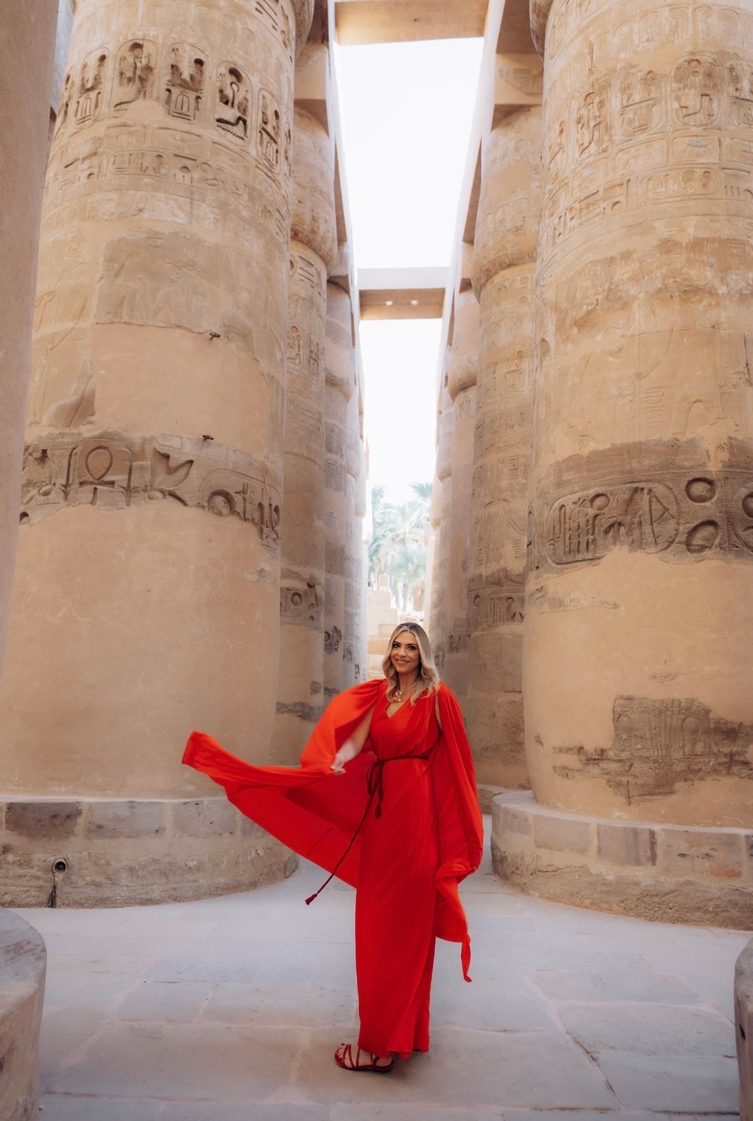 Alexandra in a flowing red dress between the towering carved columns of Karnak Temple
